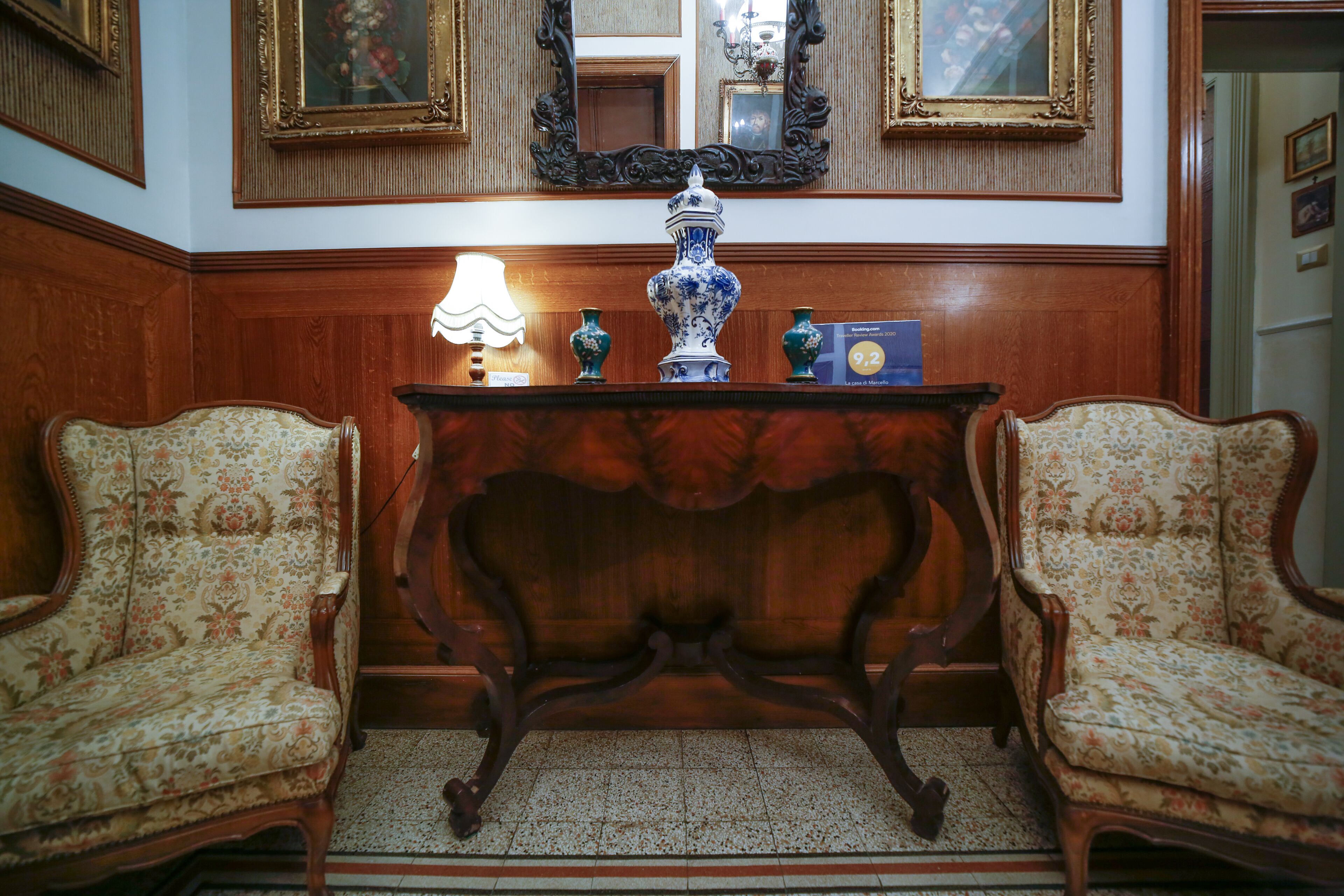 A room with two ornate chairs, a wooden console table with a vase, and a mirror on the wall.