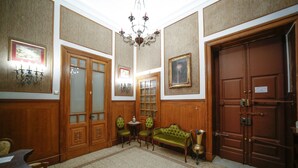 Una habitación con piso de madera, un sofá verde, una araña y una puerta grande de madera.