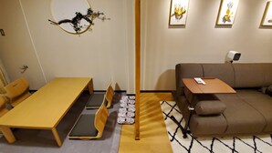 A modern hotel room with a wooden dining table, a sofa, and a small side table. There are framed artworks on the wall and a security camera mounted on the wall. - Sakuranomiya Hotel-Self Service (Osaka)