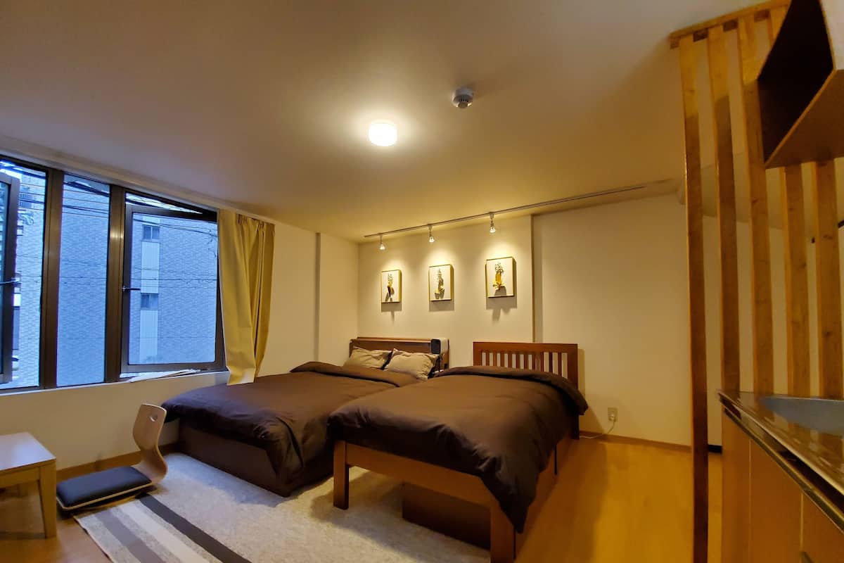 Quarto com duas camas, uma janela, uma escrivaninha e uma escada.