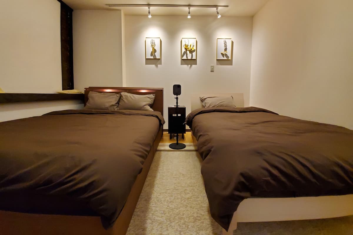 Quarto com duas camas, uma mesinha de cabeceira e três luminárias fixadas na parede.