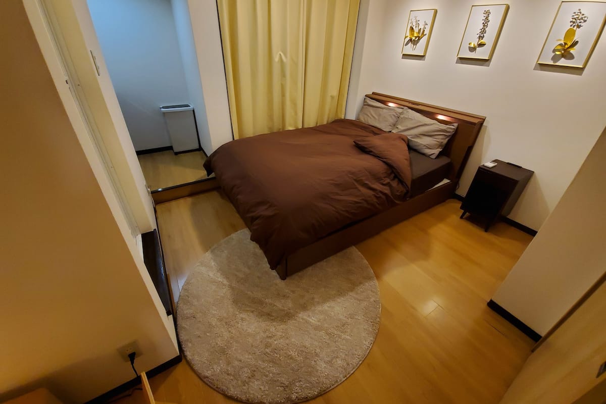 Um quarto com uma cama, um tapete redondo e dois quadros pendurados na parede.