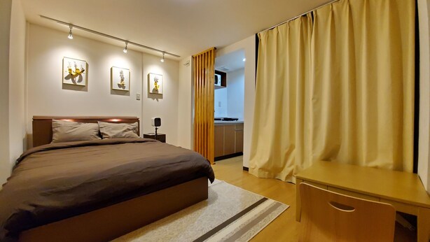 A modern hotel room with a large bed, a desk, and a kitchenette in the background. - Sakuranomiya Hotel-Self Service (Osaka)
