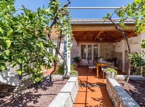A covered outdoor patio with a stone wall, a table with chairs, and potted plants.