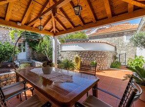 An outdoor patio with a wooden table and chairs, a stone wall, and a covered area with a wooden ceiling.