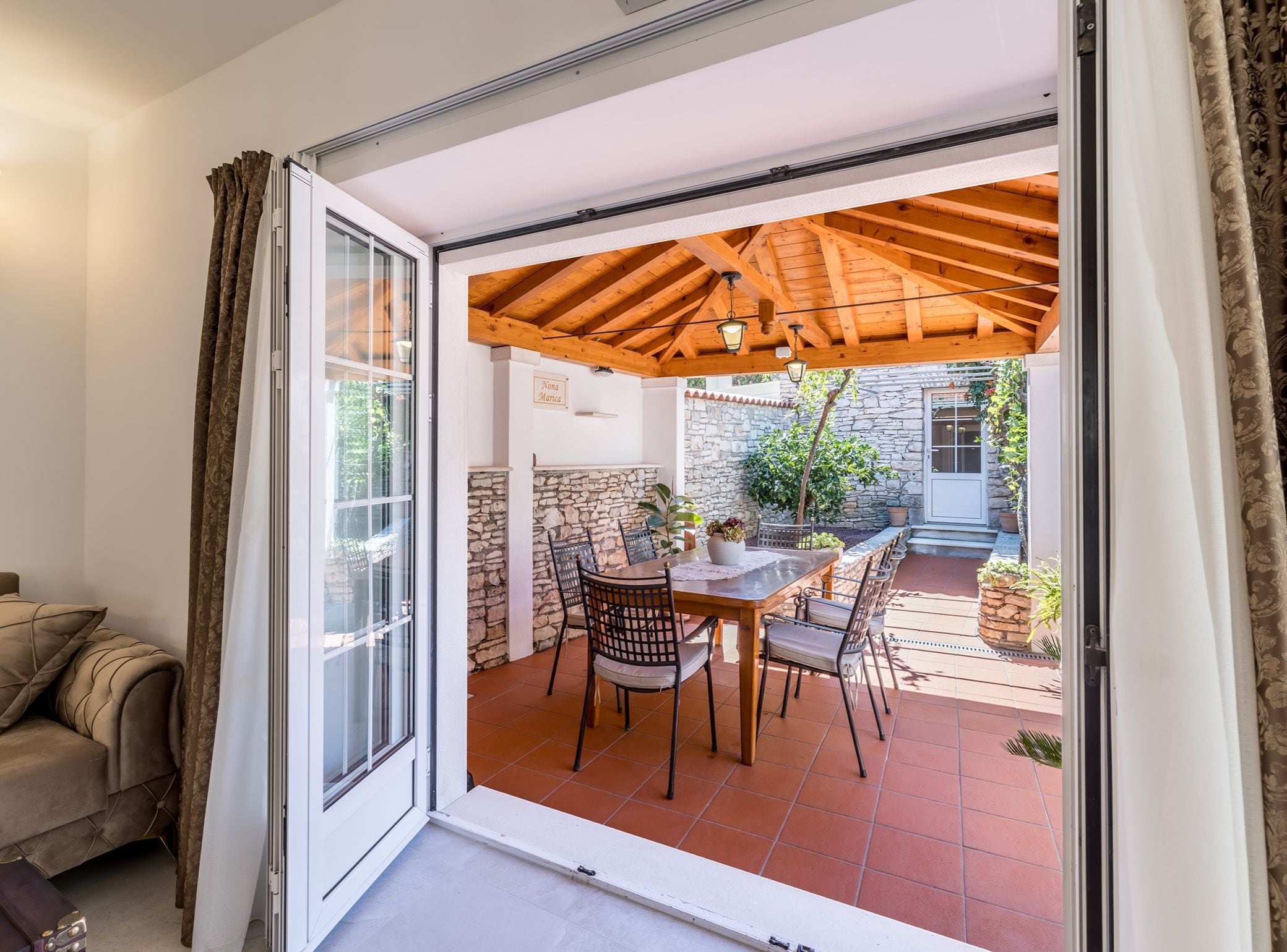 A room with a sliding glass door leading to an outdoor patio with a wooden pergola, stone wall, and a dining table with chairs.