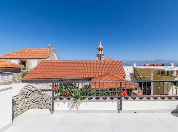 A building with a red-tiled roof, a stone wall, and a metal railing with flowers.