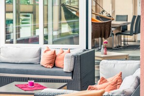 A modern outdoor seating area with a sofa and chairs, a table with a pink napkin, and a glass of drink.