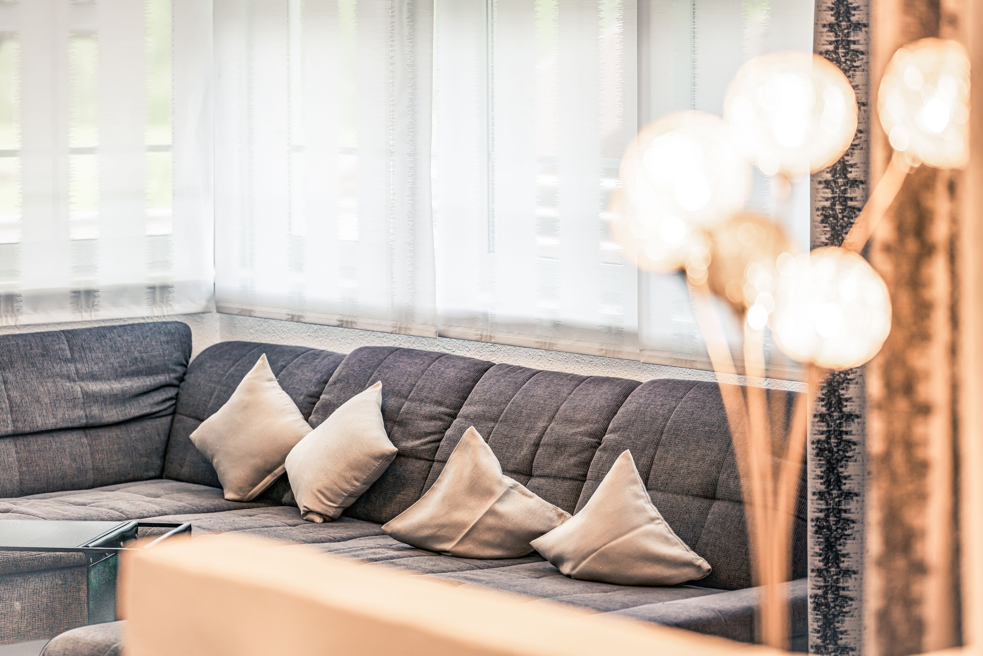 Una sala de estar moderna con un sofá gris, tres cojines beige y una mesa de centro de vidrio.