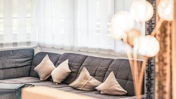 Una sala de estar moderna con un sofá gris, tres cojines beige y una mesa de centro de vidrio.
