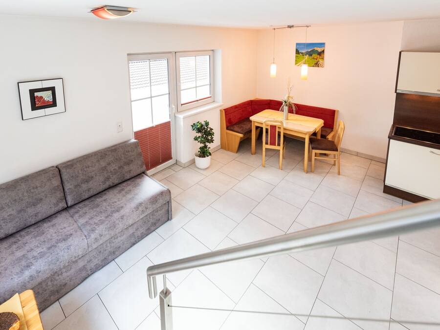 A modern living room with a grey sofa, a dining area with a red bench, and a kitchen with white cabinets.