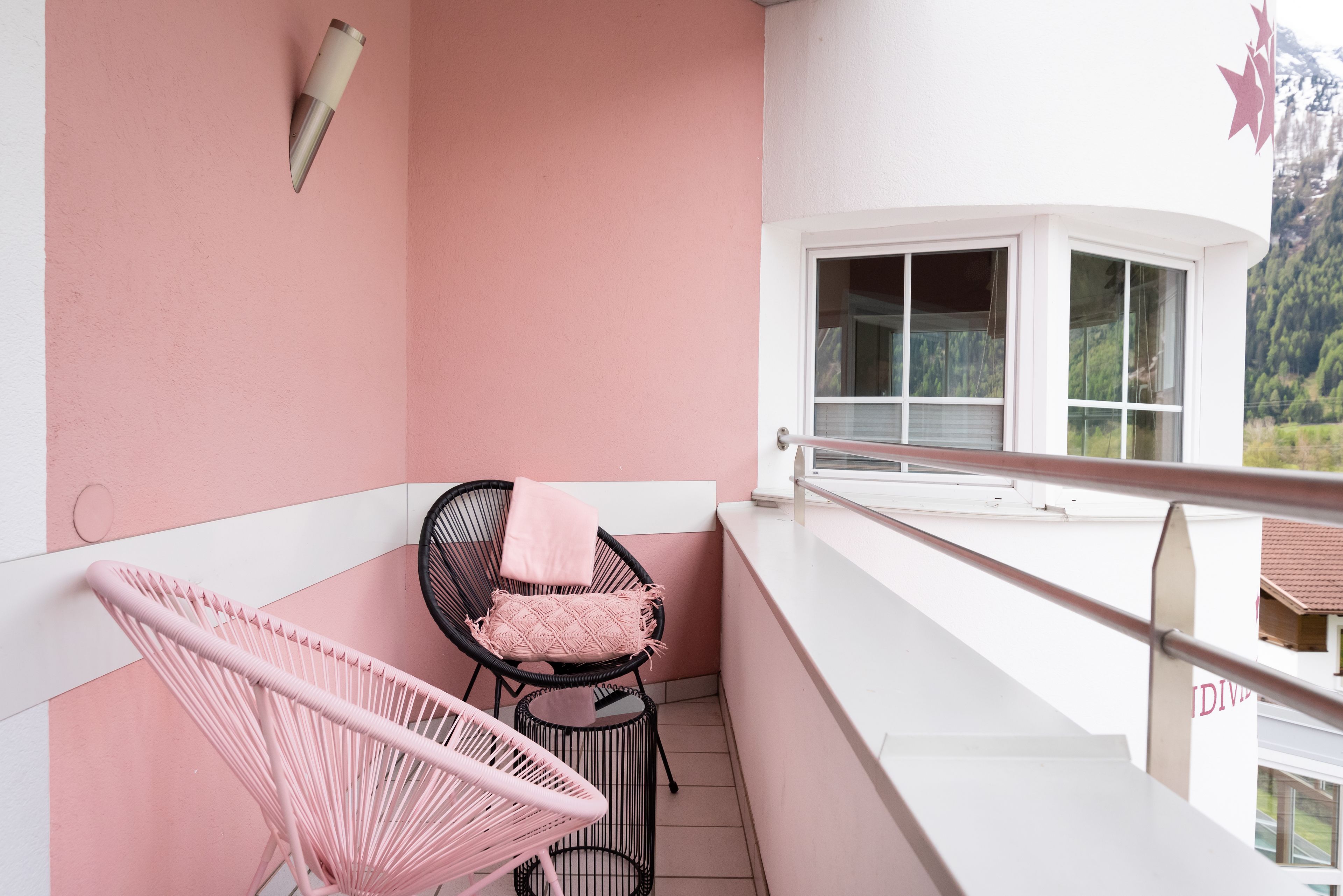 Un balcone con due sedie, una rosa e una nera, e una ringhiera bianca.