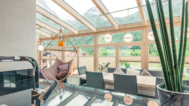 A modern kitchen with a glass dining area, a hanging chair, and a large potted plant. - Apart Relax (Laengenfeld)