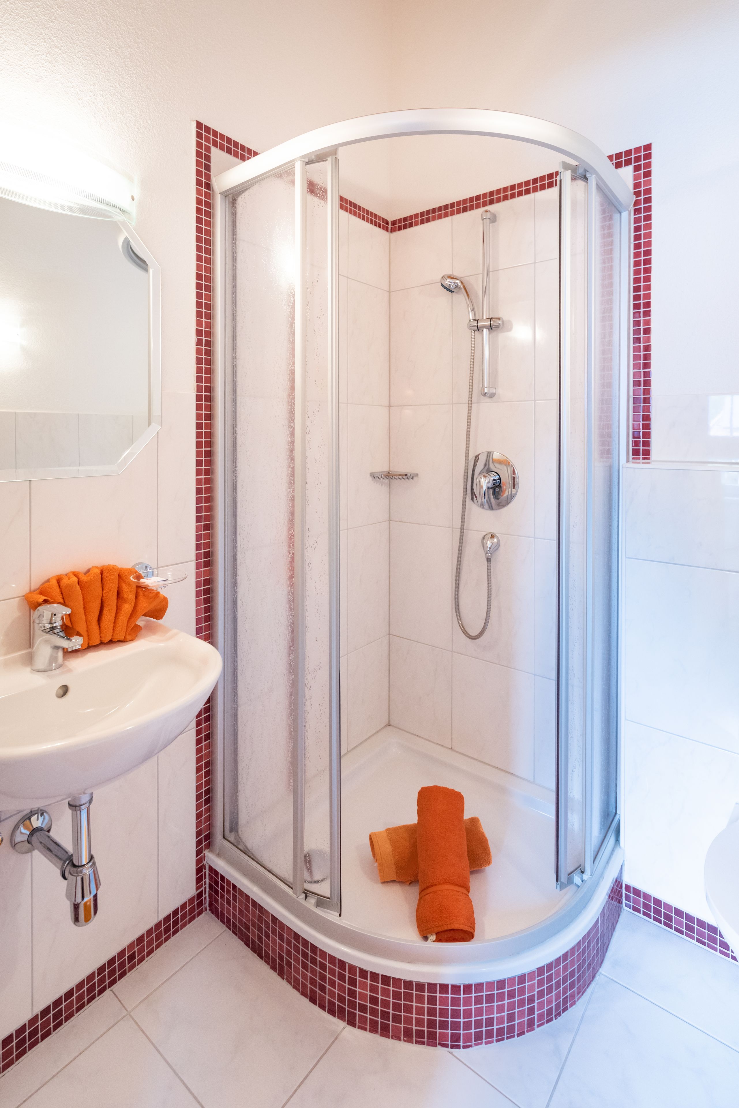 Een douche met een glazen deur, een wastafel met een chromen kraan en een handdoek op de vloer.