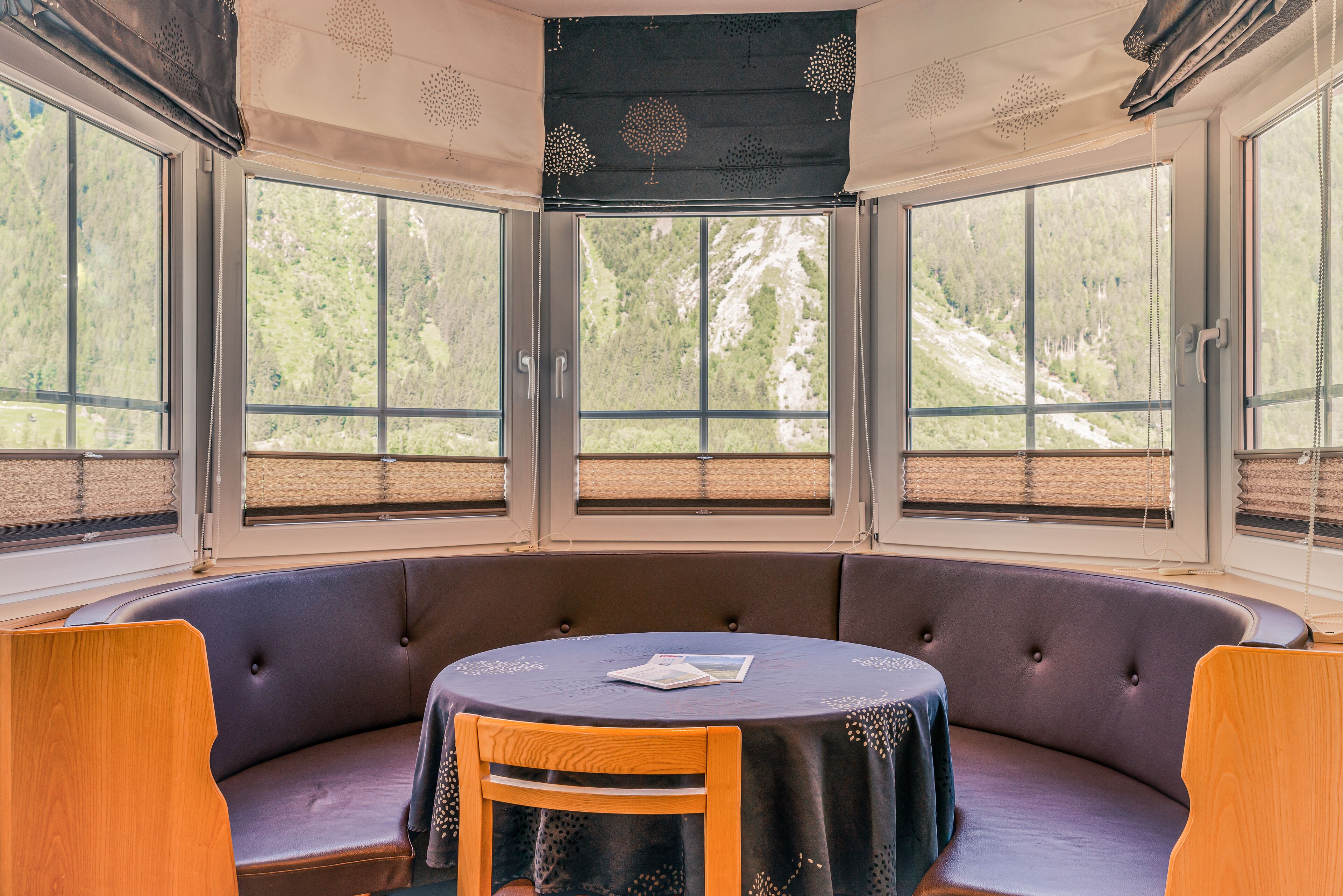 Un coin salon avec une table ronde, des sièges confortables et de grandes fenêtres donnant sur un paysage boisé.