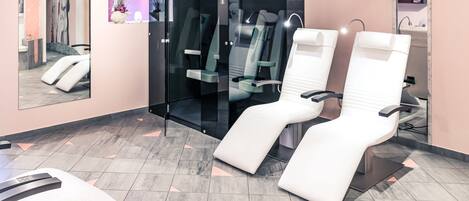 Een moderne tandartspraktijk met twee relaxstoelen, een glazen scheidingswand, en een receptiegedeelte met een spiegel en wanddecoratie.