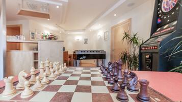 A checkered chessboard with pieces set up in the middle of a room with a dartboard and a jukebox in the background.