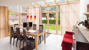 A dining area with a wooden table and chairs, a television, and a view of a garden through large glass doors. - Apart Relax (Laengenfeld)