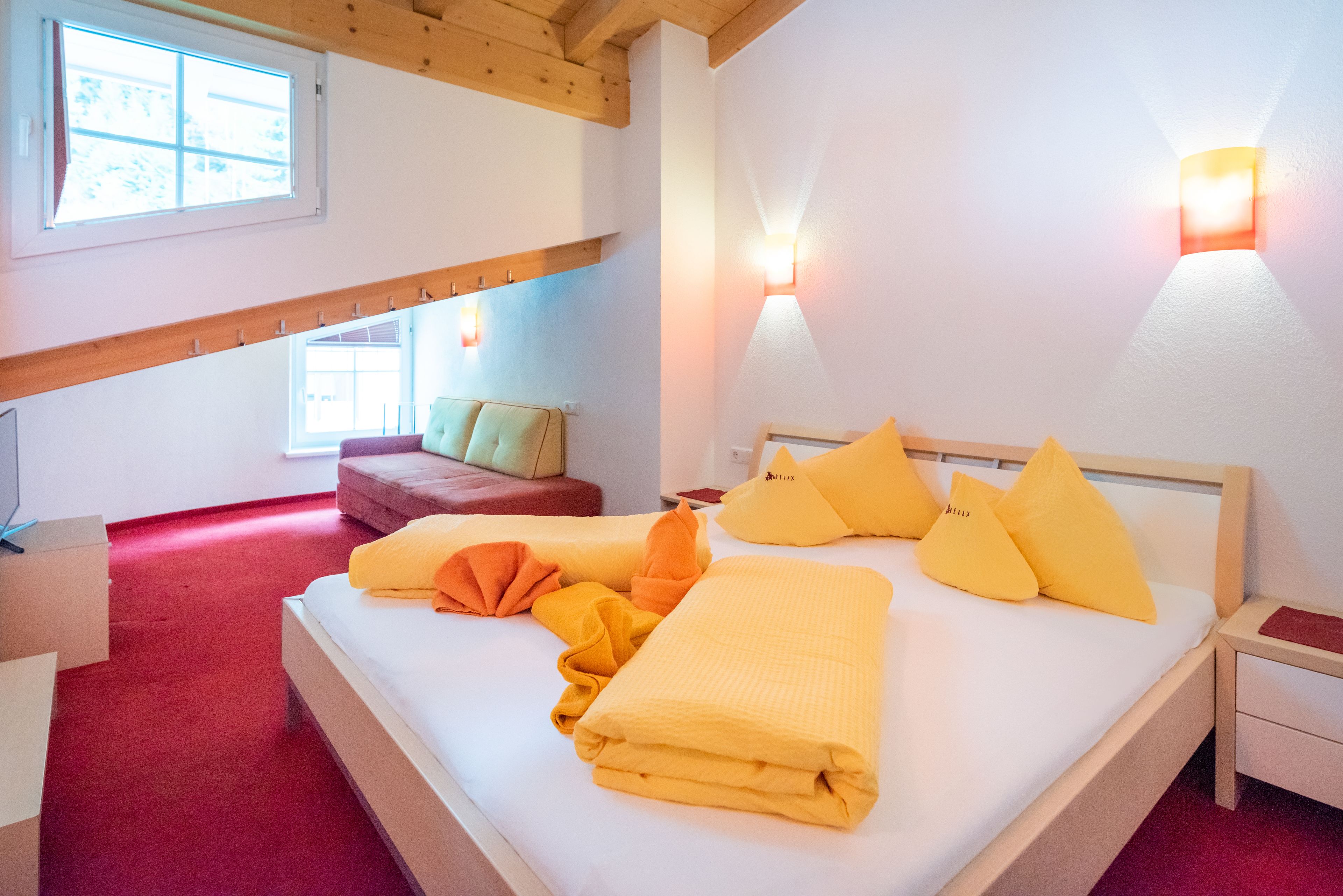 Une chambre à coucher avec un lit, des oreillers, une table de chevet, un canapé rouge et une fenêtre.