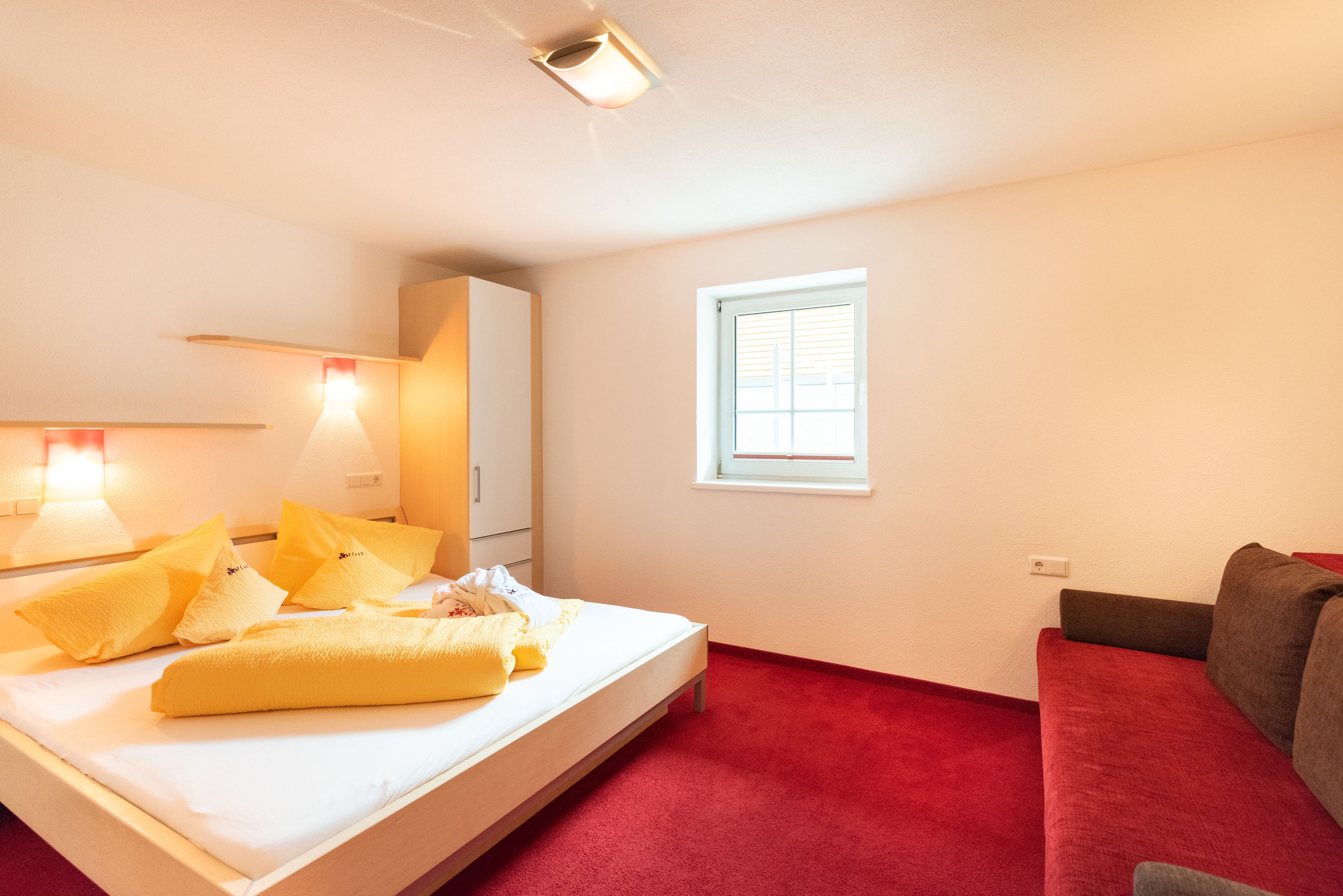 A hotel room with a bed, a red carpet, a window, and a sofa.