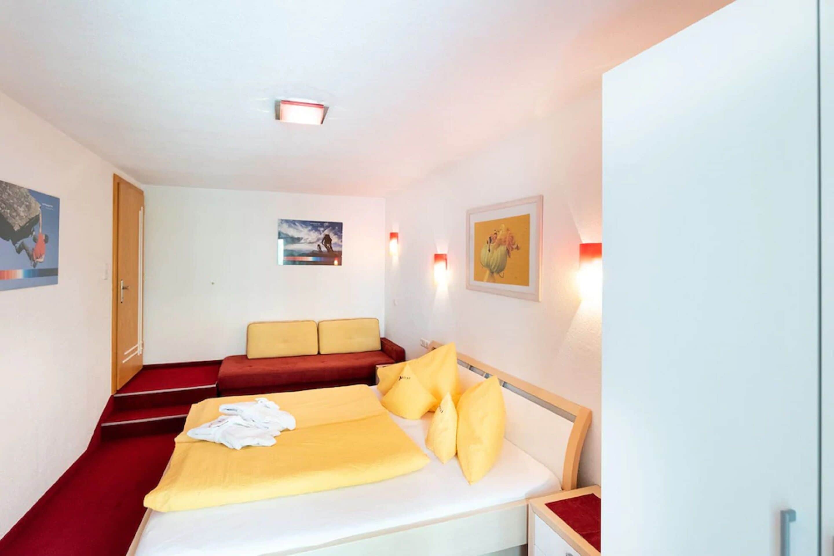 Una habitación de hotel con una cama, cojines rojos y amarillos, un sofá rojo y obras de arte en las paredes.