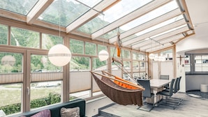 A modern kitchen with a large island, a hanging chair, and a view of a mountainous landscape through large windows. - Apart Relax (Laengenfeld)
