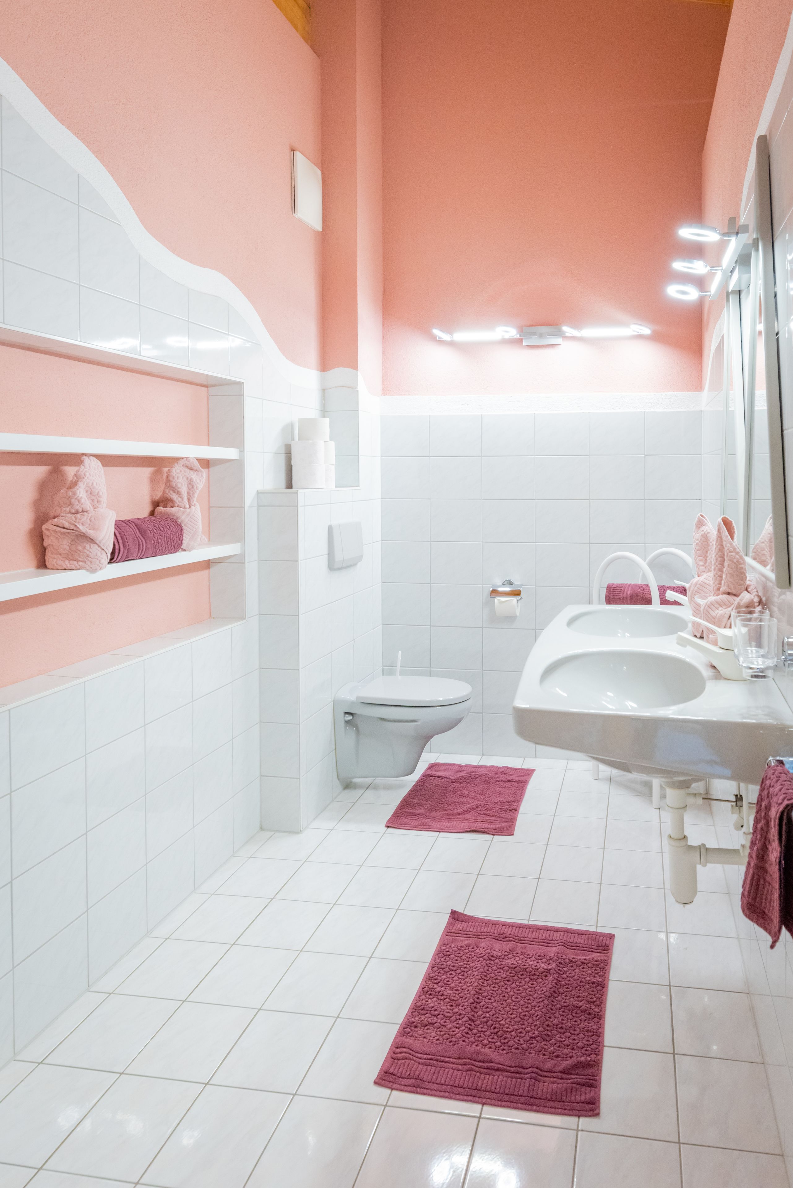 Un baño con azulejos blancos, toallas rosas, un inodoro, un lavabo y un espejo.