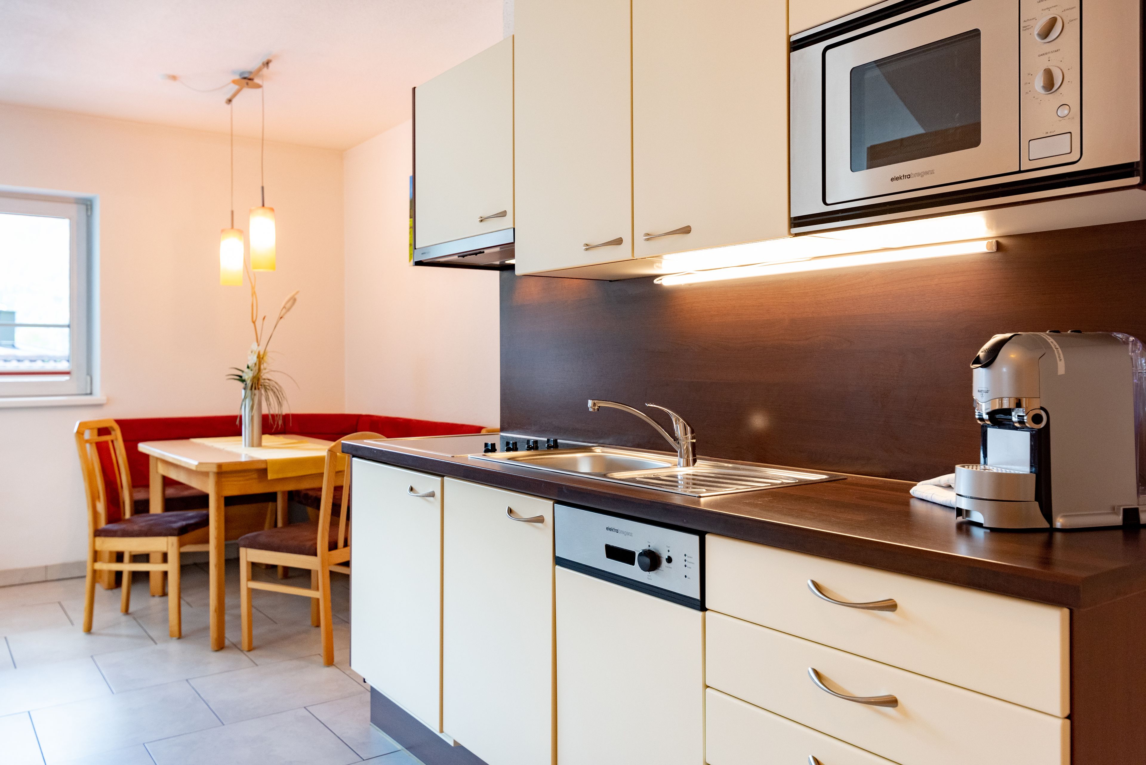 A modern kitchen with a built-in microwave, coffee machine, and dishwasher. There is a dining area with a table and chairs.