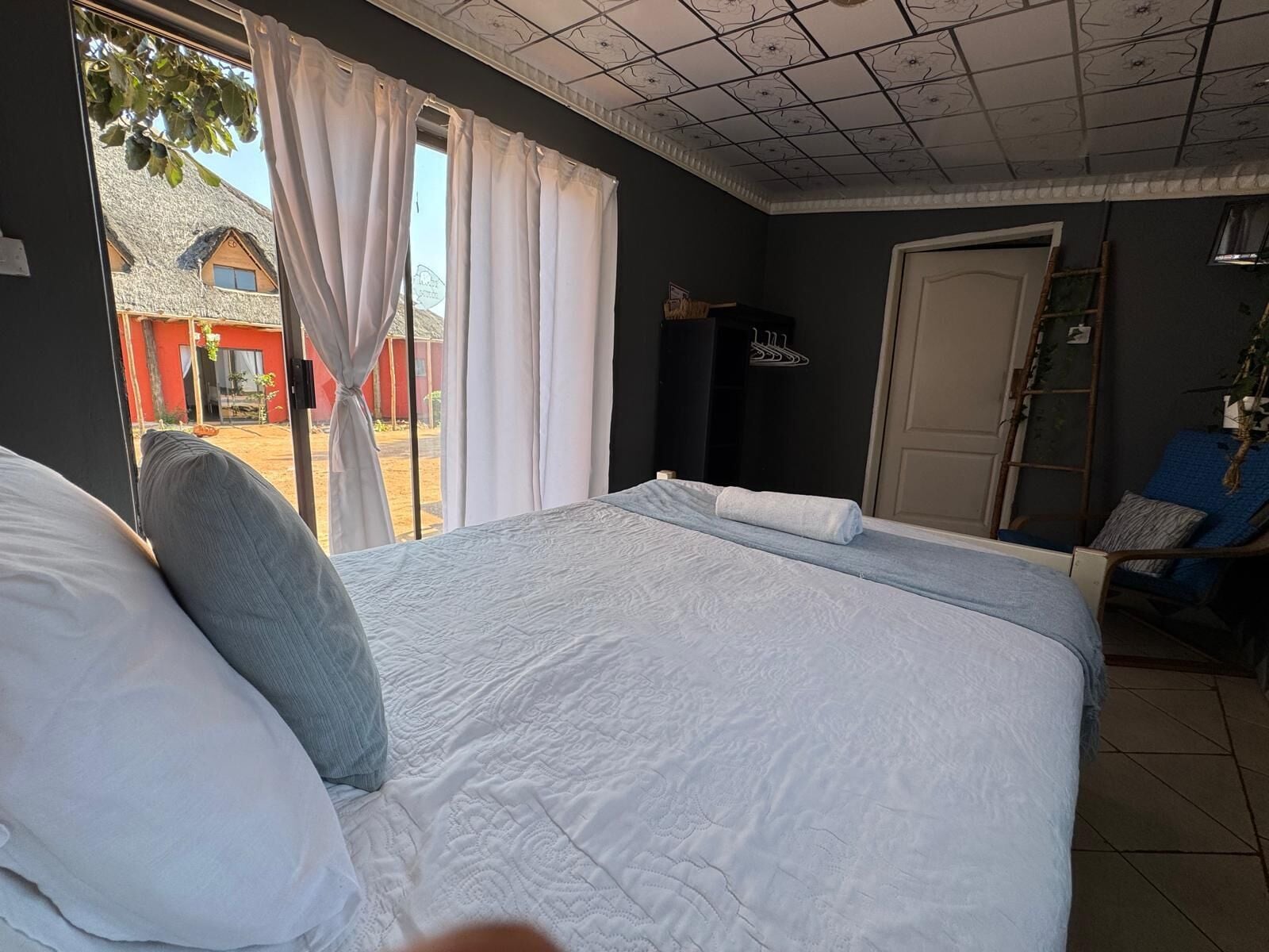 Un dormitorio con cama, una ventana con cortinas, una puerta y una silla.