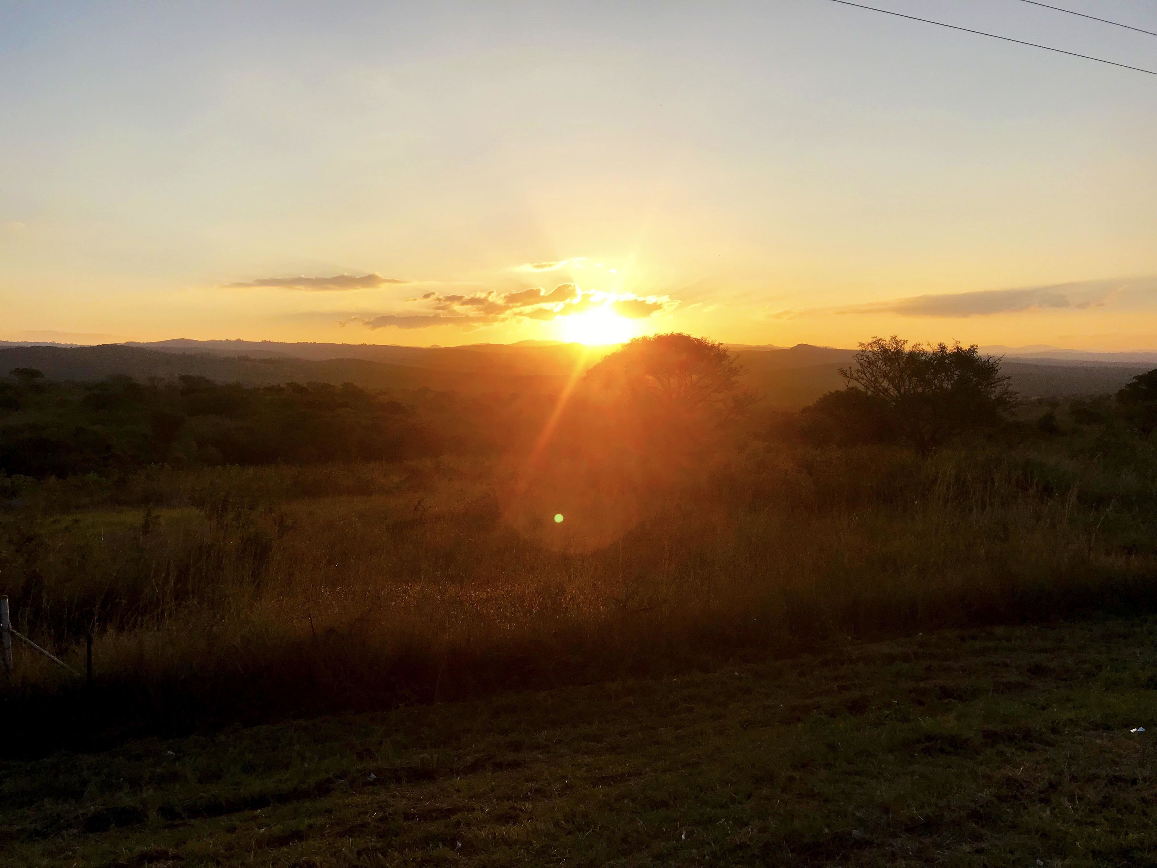 Un coucher de soleil sur un paysage verdoyant, avec des collines à l’horizon.