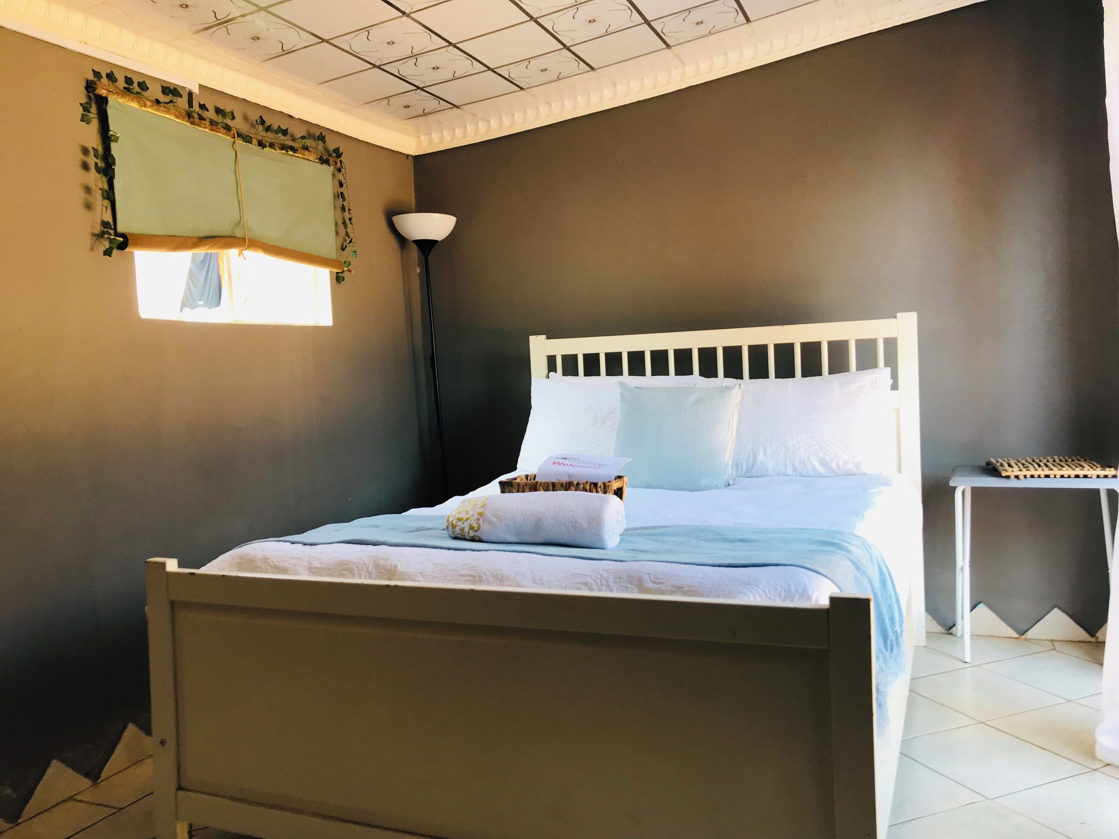 A bedroom with a bed, a bedside table, a lamp, and a window.