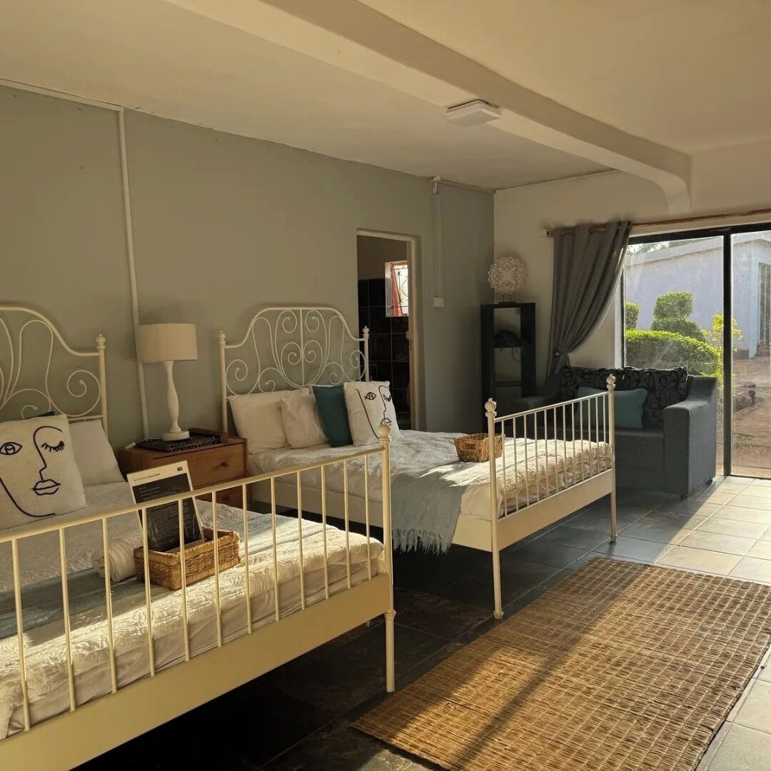 A bedroom with two beds, a sofa, and a view of the garden.