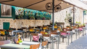 An outdoor café with tables and chairs, a stone wall, and potted plants. - Apartments Gabrieri - Studio with Sea View (2 Adults + 1 Child) (2) (Dubrovnik)