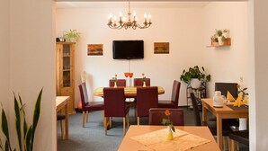 A dining area with a round table, red chairs, a chandelier, and wall-mounted TV. - Pension Dapper (Cochem)