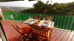A terrace with a table set for two, overlooking a hilly landscape.