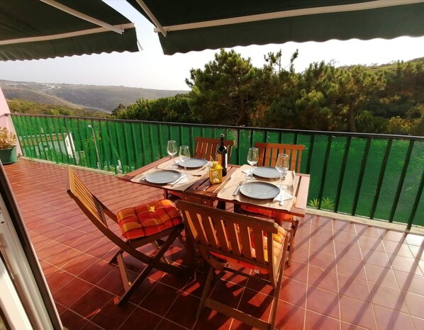 A terrace with a table set for two, overlooking a hilly landscape.