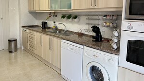 A modern kitchen with light wood cabinets, a granite countertop, a dishwasher, a washing machine, and a microwave.