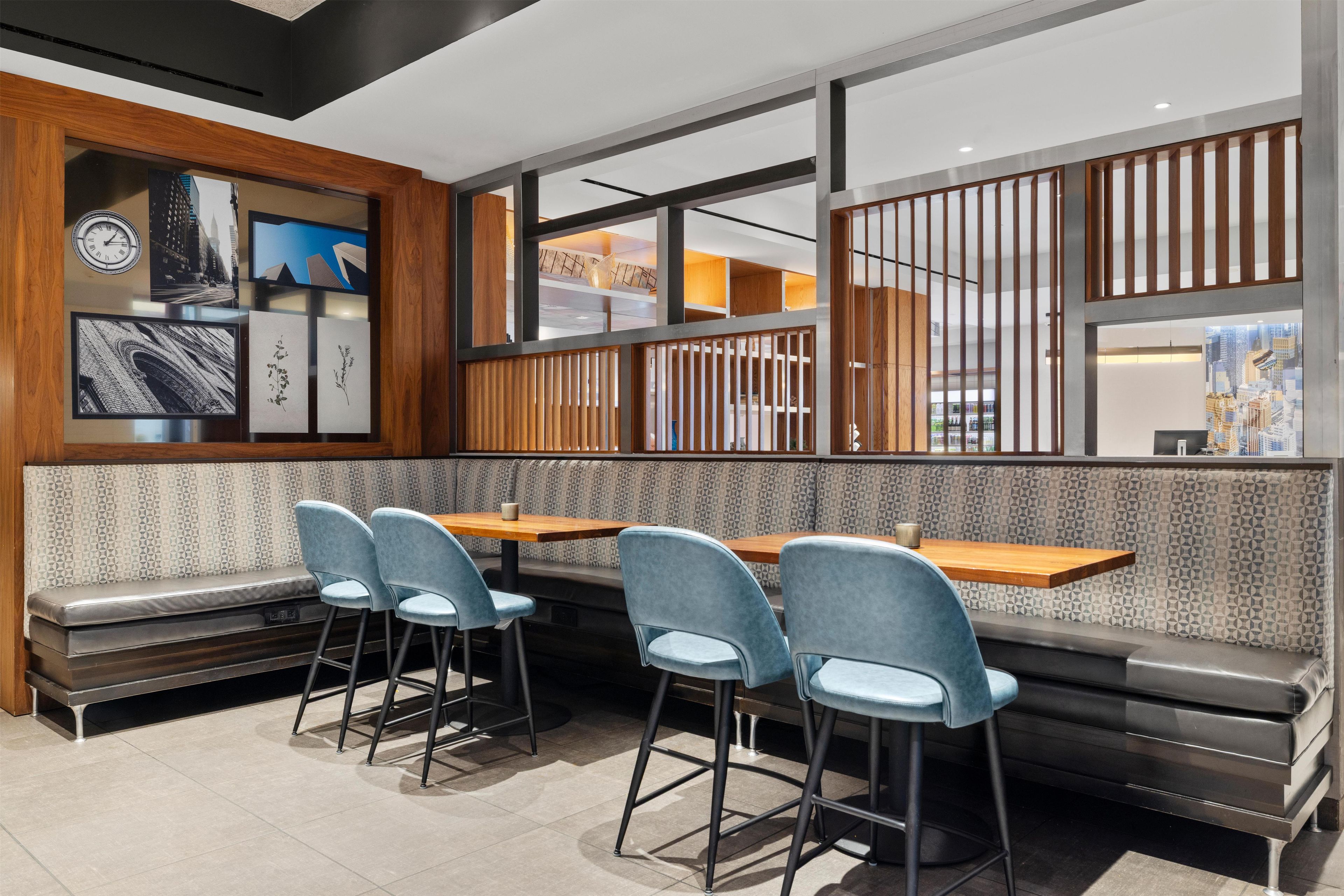 Ein modernes Restaurant mit hoher Decke, verschiedenen Sitzgelegenheiten wie Sitzecken und Barhocker sowie einer Wand mit gerahmten Bildern.