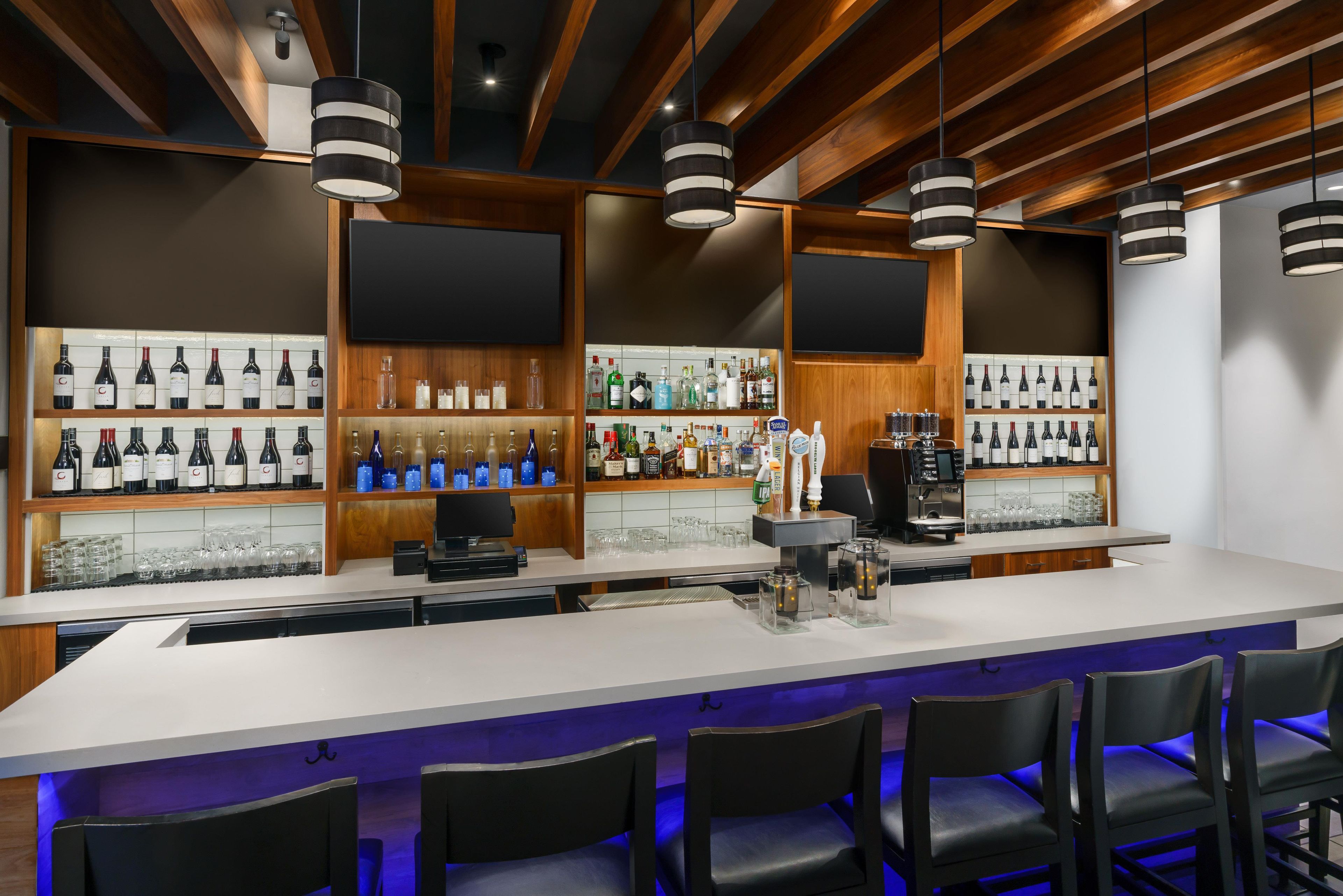 A bar area with a long counter, multiple shelves of bottles, and bar stools.