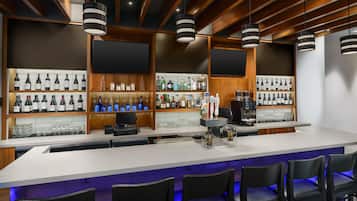 A bar area with a long counter, multiple shelves of bottles, and bar stools.