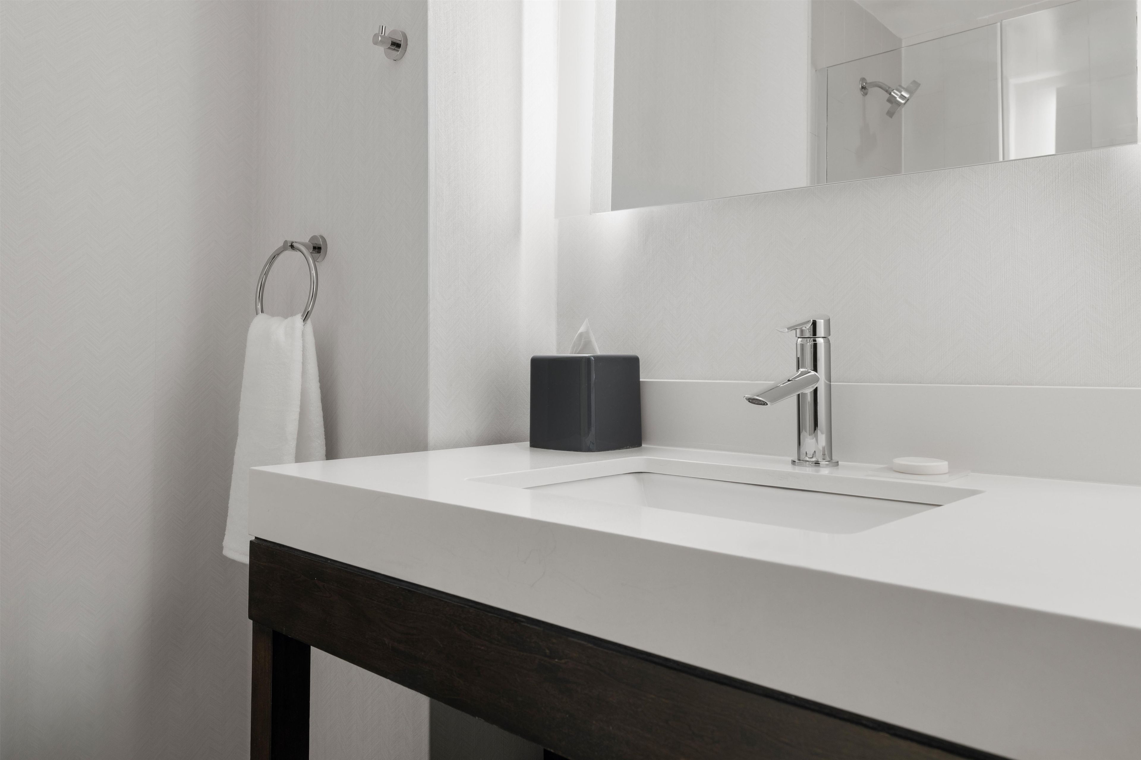 A modern bathroom with a white sink, a dark wooden bench, a towel ring, and a mirror.