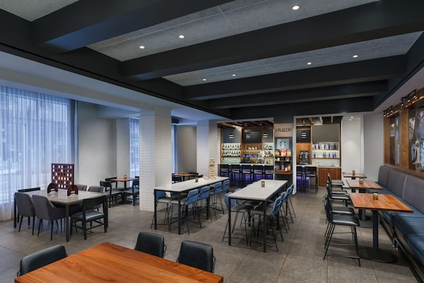 A modern restaurant with multiple seating areas, including tables and booths, and a bar area with shelves of bottles. - Hyatt Place New York City/Times Square (New York)