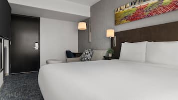 A hotel room with a large bed, a desk, a chair, a lamp, and a painting on the wall.