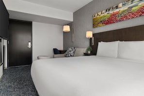 A hotel room with a large bed, a desk, a chair, a lamp, and a painting on the wall. - Hyatt Place New York City/Times Square (New York)