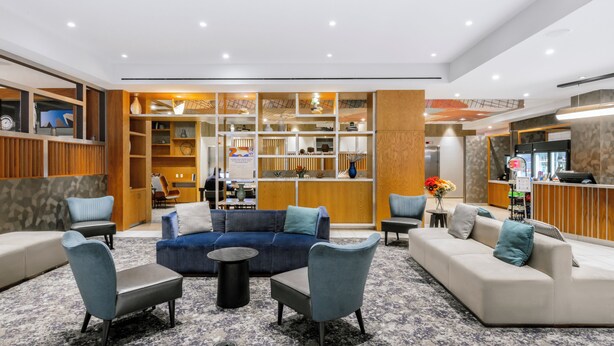 Eine moderne Hotelhalle mit einem blauen Sofa, grauen Sesseln und einer Rezeption.