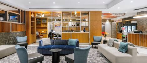 A modern hotel lobby with a blue sofa, grey armchairs, and a reception desk.