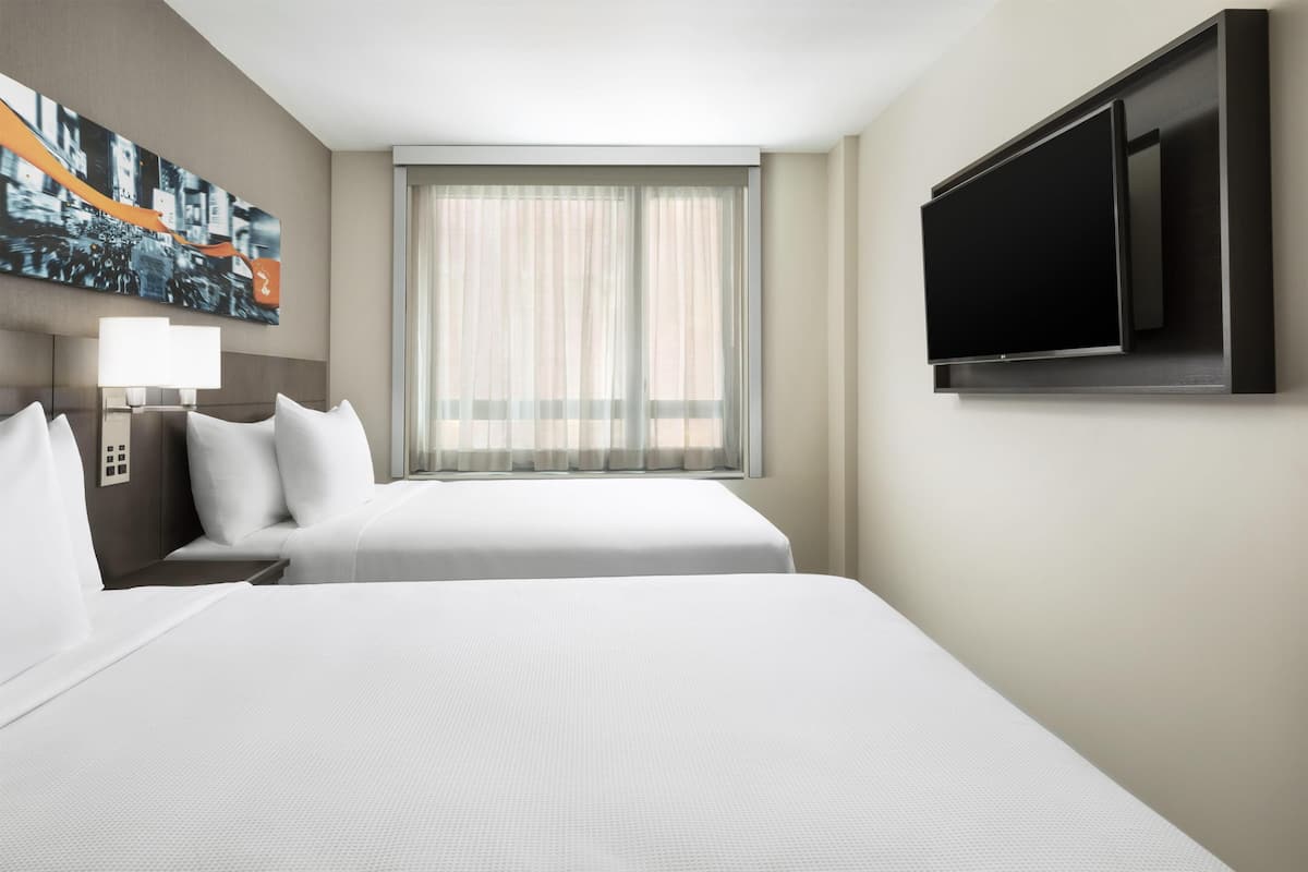Ein Hotelzimmer mit Bett, Fernseher, Fenster mit Vorhängen und einem Bild an der Wand.