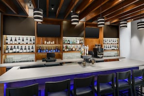 A bar area with a long counter, multiple shelves of bottles, and bar stools. - Hyatt Place New York City/Times Square (New York)