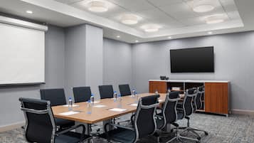 A conference room with a long table, black chairs, a whiteboard, and a flat-screen TV on the wall.