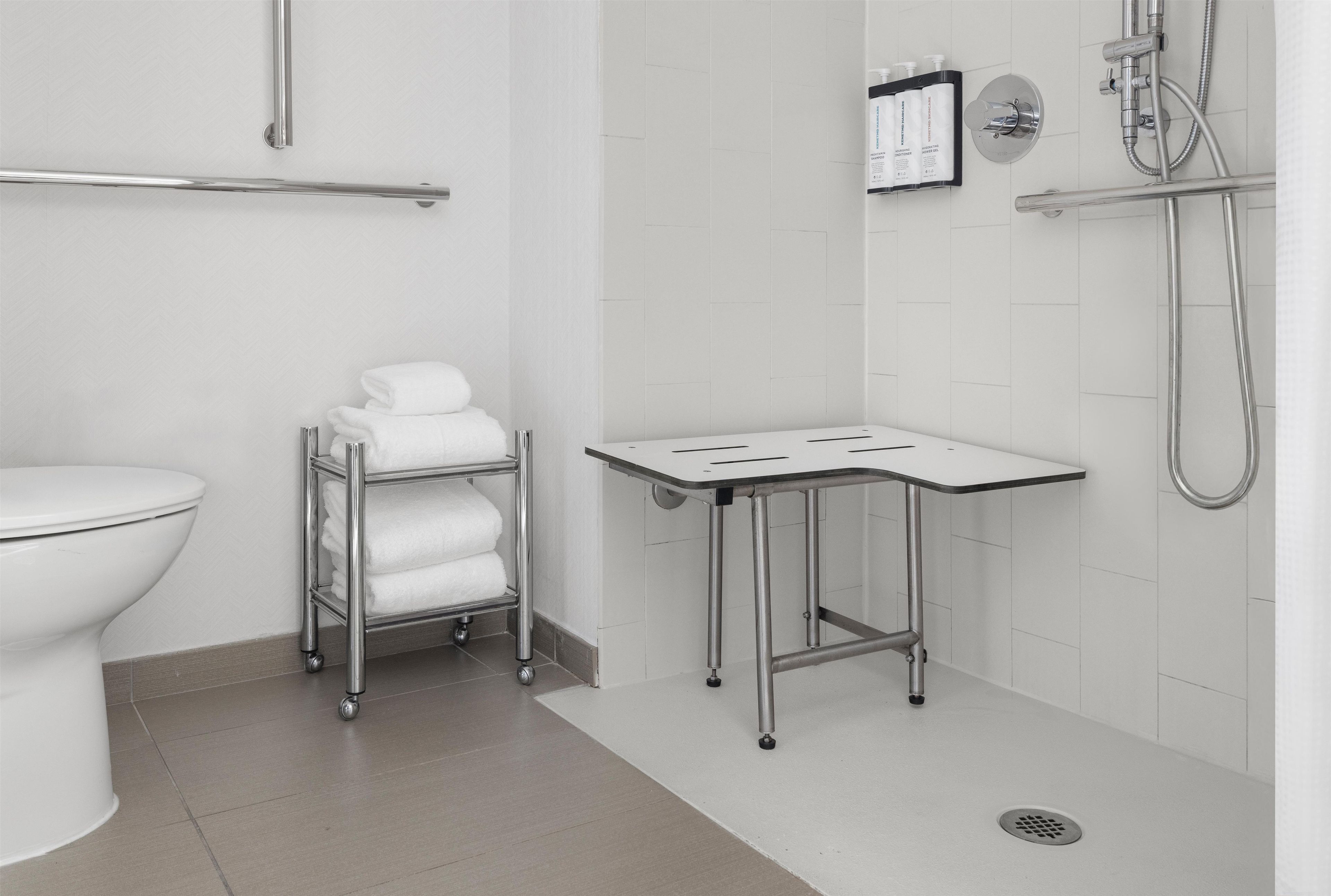 A modern bathroom with a toilet, a towel rack with folded towels, a small table, and a shower area with a handheld showerhead.
